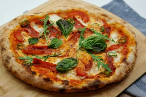 Pizza maison avec une pâte à pizza préparée la veille, garnie de tomates, mozzarella, roquette, basilic, piments et salami.