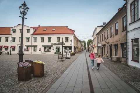 Två flickor springer glatt längs en kullerstensgata i Vadstena. Besök Vadstena för en charmig upplevelse.