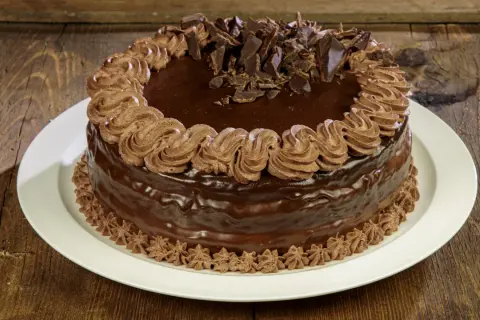 Torta compleanno cioccolato e panna, ricoperta di glassa lucida e decorata con riccioli di panna e scaglie di cioccolato.