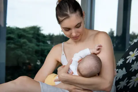 Delikatny moment karmienia piersią. Mama z miłością patrzy na swoje dziecko, które pije mleko z piersi.