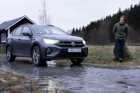 Grå VW Taigo står på en isig väg nära en röd stuga. En man står lutad mot en sten i bakgrunden.