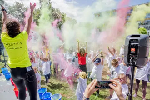 Kolorowy festiwal proszków w Kołobrzegu! Dzieci w białych koszulkach rzucają kolorowymi proszkami, tworząc radosną atmosferę. To świetne kołobrzeg atrakcje dla dzieci.