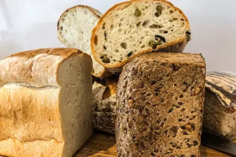 Kilka rodzajów chleba, w tym bochenek z oliwkami i chleb pełnoziarnisty.