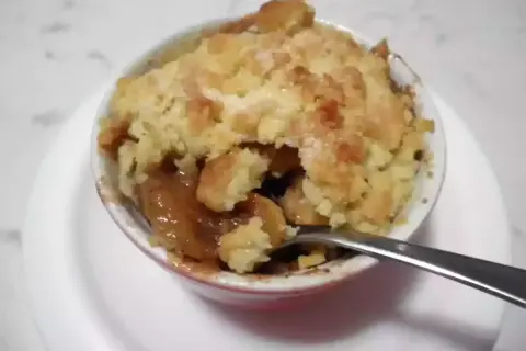 Un delizioso crumble di mele appena sfornato, con la crosta dorata e il ripieno succoso. Una forchetta è immersa nel dolce.