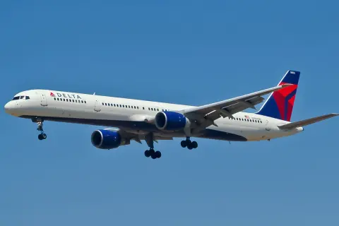 Boeing 757-300 linii Delta z wysuniętym podwoziem zbliża się do lądowania na tle błękitnego nieba.