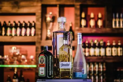 Butelka Jägermeister, Absolut, El Jimador i Hypnotiq. Różne rodzaje alkoholi na półce barowej.