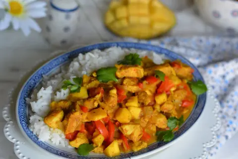 Pyszny kurczak z mango po tajsku, podany z ryżem. Aromatyczne kawałki kurczaka, słodkie mango i papryka w złocistym sosie curry.