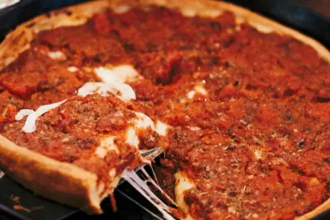Ein Stück einer tiefen Chicago Style Pizza mit geschmolzenem Käse wird herausgehoben.