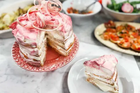 En vacker rabarberkompott tårta med rosa glasyr och dekorationer. En bit är upplagd på en tallrik.