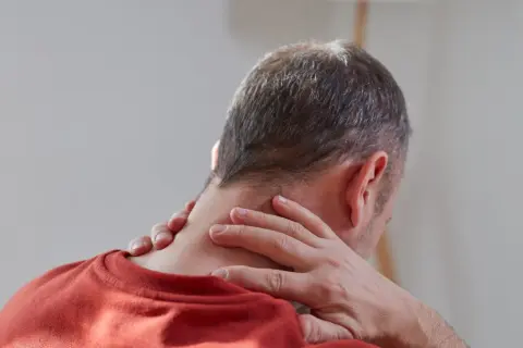 Mężczyzna masuje kark, szukając ulgi w bólu. Czy to początek problemu, jak zlikwidować wdowi garb?