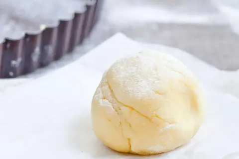 Une boule de pâte sucrée amande, saupoudrée de sucre glace, prête à être utilisée dans un moule à tarte.