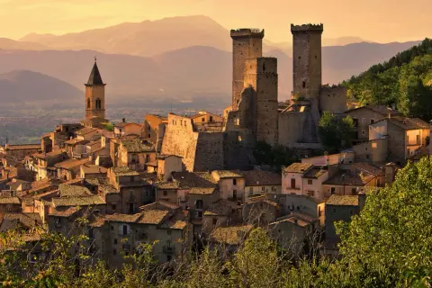 Borghi da visitare in Abruzzo: un castello medievale domina un villaggio arroccato, con torri imponenti e case in pietra sotto un cielo dorato.
