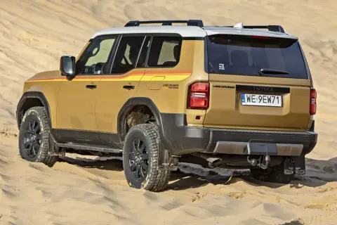 Złoty Land Cruiser z kolorowymi pasami na boku, gotowy na przygodę w piaskach pustyni, niczym potężna sequoia w krajobrazie.