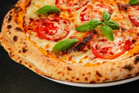 Zbliżenie na idealną pizzę z pomidorami, serem i bazylią, z przypieczonymi brzegami.