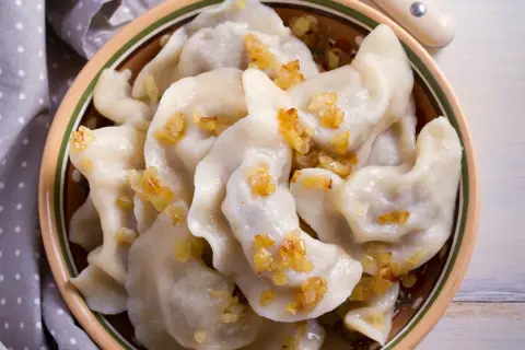 Pierogi chłopskie z podsmażoną cebulką w glinianej misce.