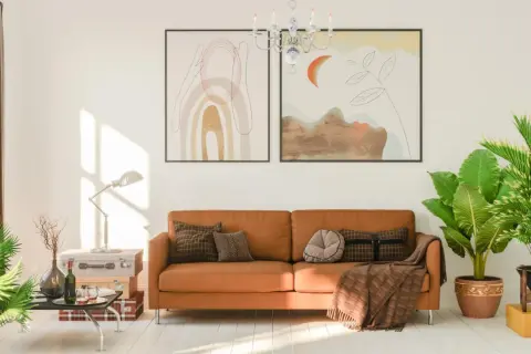 Ein gemütliches Wohnzimmer mit einem orangefarbenen Sofa, das mit Kissen und einer Decke dekoriert ist. Die Sofa-Farbe passt gut zu den Pflanzen und Bildern.
