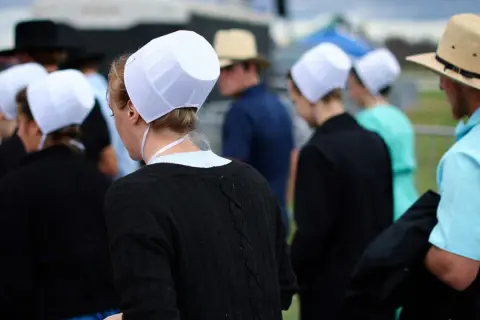 Människor i traditionella kläder, som påminner om amish i Sverige, med vita hättor och hattar.