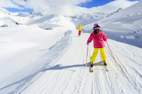 Bambini imparano a sciare su piste da sci per principianti, con montagne innevate sullo sfondo.