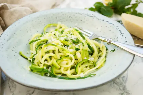 Ein Teller mit Zoodles, einem leichten Zucchini-Nudel-Gericht, bestreut mit Parmesan. Ein einfaches und gesundes Zoodles Rezept.