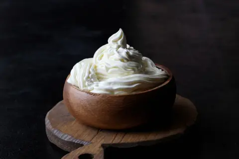 Kremowy mascarpone w drewnianej miseczce, idealny do deserów. Warto sprawdzić mascarpone kcal przed przygotowaniem słodkości.
