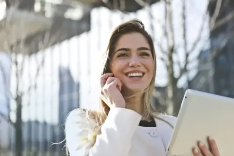 Donna sorridente con tablet, forse sta per uscire prima dal lavoro senza permesso, con un'aria di gioia e libertà.