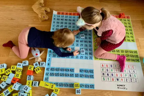 Dwie dziewczynki uczą się czytać, układając litery na planszy. Idealna zabawa, jak nauczyć dziecko czytać 6 latka.