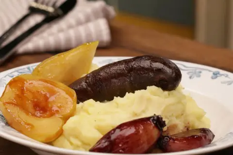 Herzhaftes Gericht mit Kartoffelpüree, dunkler Wurst, karamellisierten Zwiebeln und Birnenstücken – eine köstliche Kombination aus Himmel und Erde.