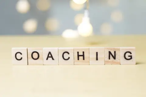 Drewniane klocki z literami układają słowo "COACHING". To właśnie kim jest coach – osoba wspierająca rozwój.