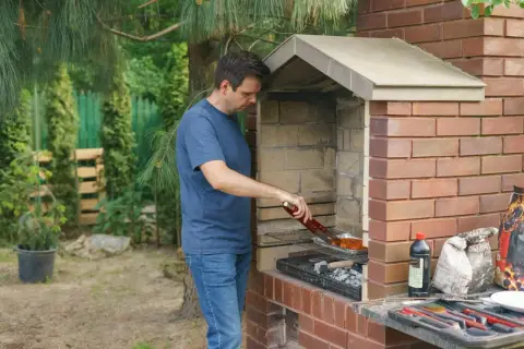 Mężczyzna grilluje mięso przy ceglanym kominie. Zastanawiam się, ile cegieł na komin zużyto do jego budowy.