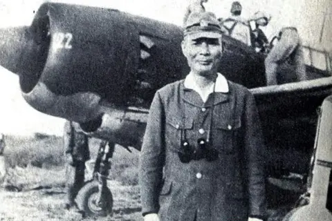 En japansk kamikaze pilot står framför ett flygplan.
