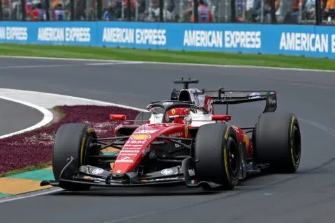 Un'auto di F1 in gara, con livrea rossa Ferrari, sfreccia in curva. La pubblicità "American Express" fa da sfondo a questa emozione da vedere in TV.