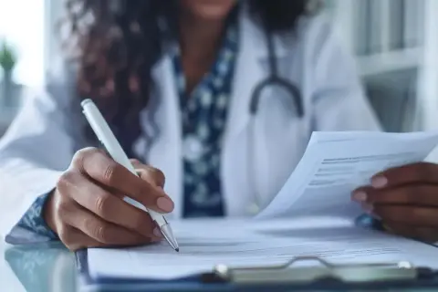 Lekarz w białym kitlu z długopisem w dłoni analizuje dokumenty. Ważne skierowanie do poradni urologicznej to klucz do dalszej diagnostyki.