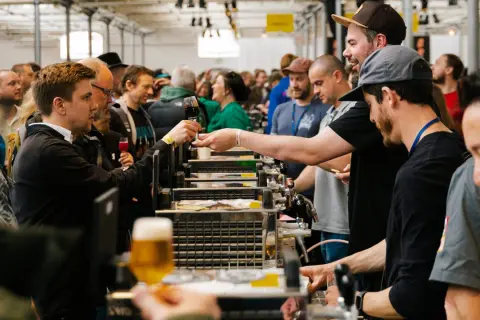 Folla a un evento di degustazione di birra a Mikkeller Copenhagen. Un uomo porge un bicchiere di birra scura.