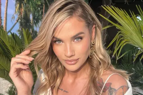 Karolina Gilon z burzą blond włosów i tatuażami na ramieniu, otoczona palmami. Ciekawe, ile lat ma Karolina Gilon?