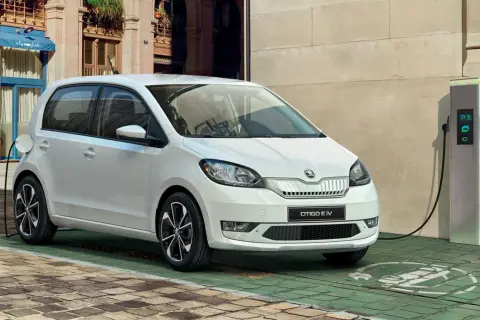Biały Skoda Citigo e IV ładuje się przy stacji ładowania na brukowanej uliczce, gotowy na miejskie przygody.