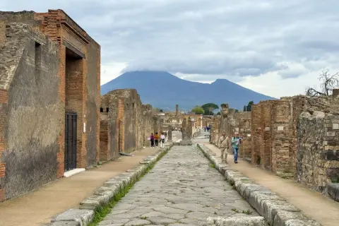 Antigua calle empedrada en el parque arqueológico de Pompeya, con ruinas a ambos lados y el Vesubio al fondo.