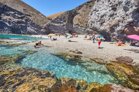 Gente disfrutando en la playa del desierto de Carboneras, con aguas cristalinas y rocas.