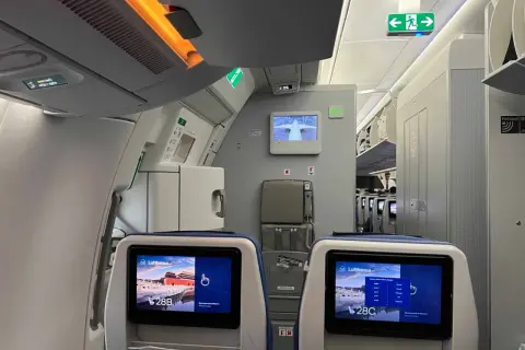 Blick in ein Flugzeug, wo man bequem sitzen kann. Die Bildschirme zeigen die Sitzplätze 28B und 28C.
