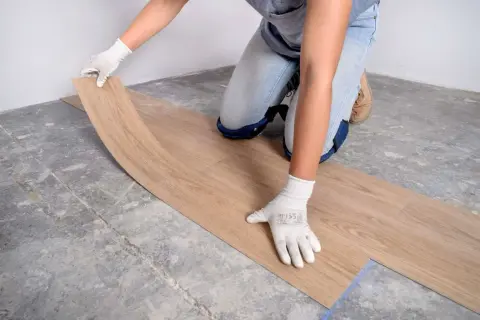 Manos enguantadas colocando una tabla de suelo vinílico sobre un suelo de hormigón.