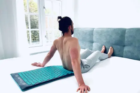 Man zit op een spijkermat, genietend van de ontspanning. De vraag is: hoe lang op spijkermat liggen voor optimaal effect?