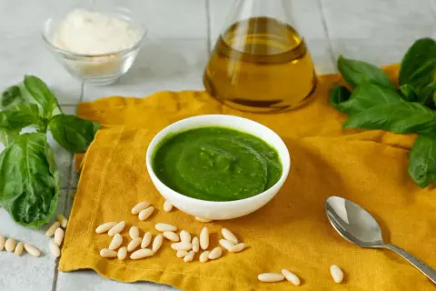 Pesto fresco in una ciotola bianca, con ingredienti per una ricetta pesto semplice: basilico, pinoli, olio d'oliva e parmigiano grattugiato.