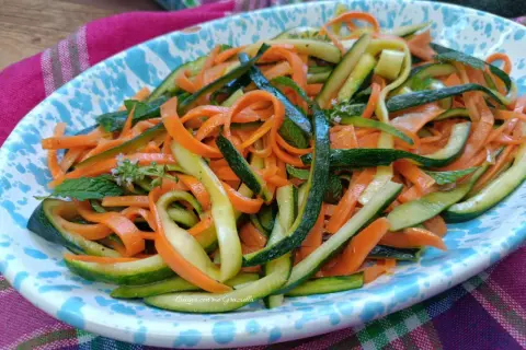 Deliziose zucchine alla julienne con carote, guarnite con menta fresca, servite su un piatto colorato.