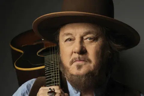 Mężczyzna w kapeluszu z gitarą, uosobienie Dire Straits Legacy.