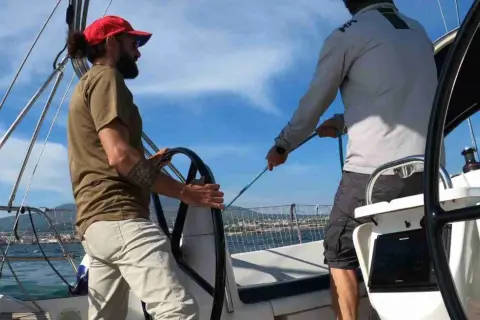 Due uomini in barca a vela, uno al timone, l'altro che regola le cime. Il **significato** di strambare è cambiare rotta.
