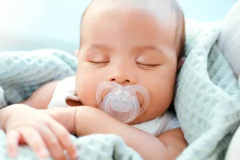 A peaceful newborn sleeps soundly, a pacifier in their mouth. This image shows that newborns do use pacifiers for comfort.