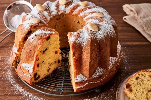 Ein köstlicher Gugelhupf-Kuchen mit Rosinen und Mandeln, bestäubt mit Puderzucker. Der Gugelhupf-Kuchen geht nicht aus der Form, aber ein Stück wurde bereits herausgeschnitten.