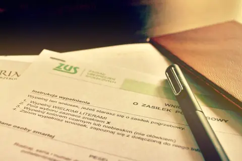Wniosek o zasiłek pogrzebowy ZUS. Dokumenty i długopis na biurku sugerują formalności związane ze śmiercią za granicą.