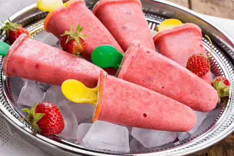 Erfrischendes Erdbeer-Eis am Stiel selber machen. Auf einem Silbertablett mit Eiswürfeln und frischen Erdbeeren serviert.