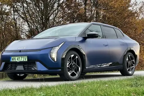 Niebieski kia sedan z matowym wykończeniem, zaparkowany na tle jesiennych drzew.
