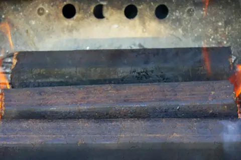 Drei Braunkohlebriketts brennen im Kaminofen. Die Flammen lodern um die Briketts.